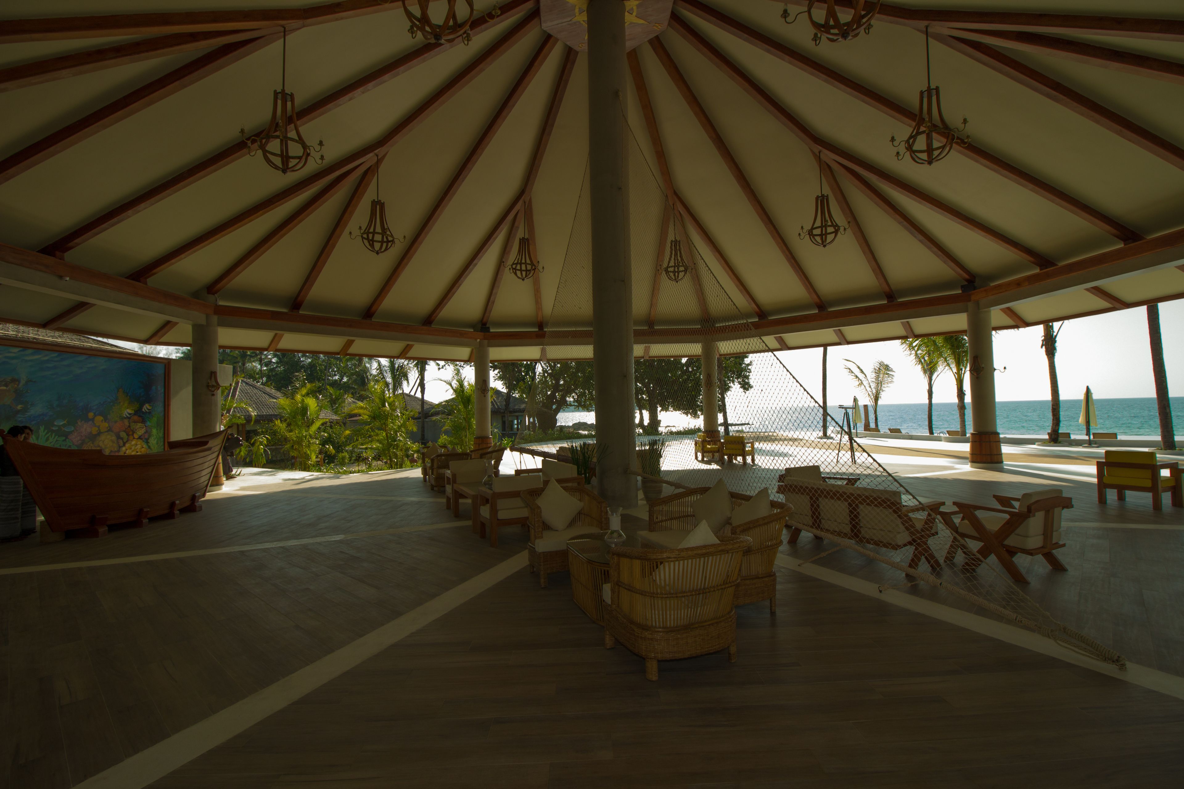 Un área de estar al aire libre cubierta con muebles de mimbre y luces colgantes, con vistas a la playa.