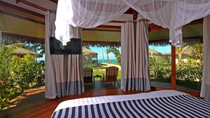 Un dormitorio con una cama grande, cortinas y vistas a un jardín tropical y al océano.