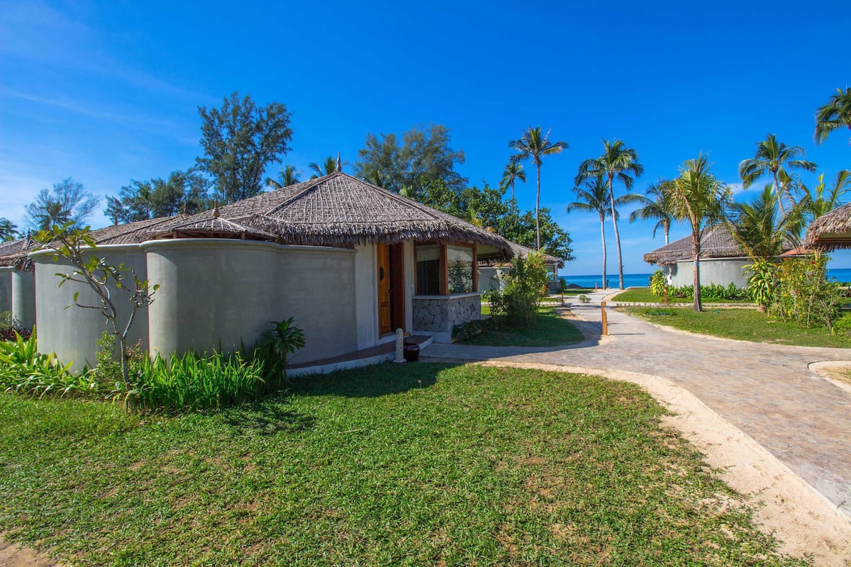 A beachfront property with a thatched-roof building, a paved walkway, and palm trees.