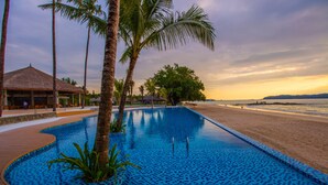 Una piscina con borde de azulejos, rodeada de palmeras y una terraza de madera.