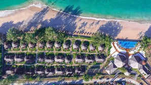 Vista aérea de un complejo turístico con acceso a la playa, varias cabañas y una piscina.