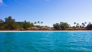 Un resort en la playa con aguas turquesas cristalinas, palmeras y cabañas.