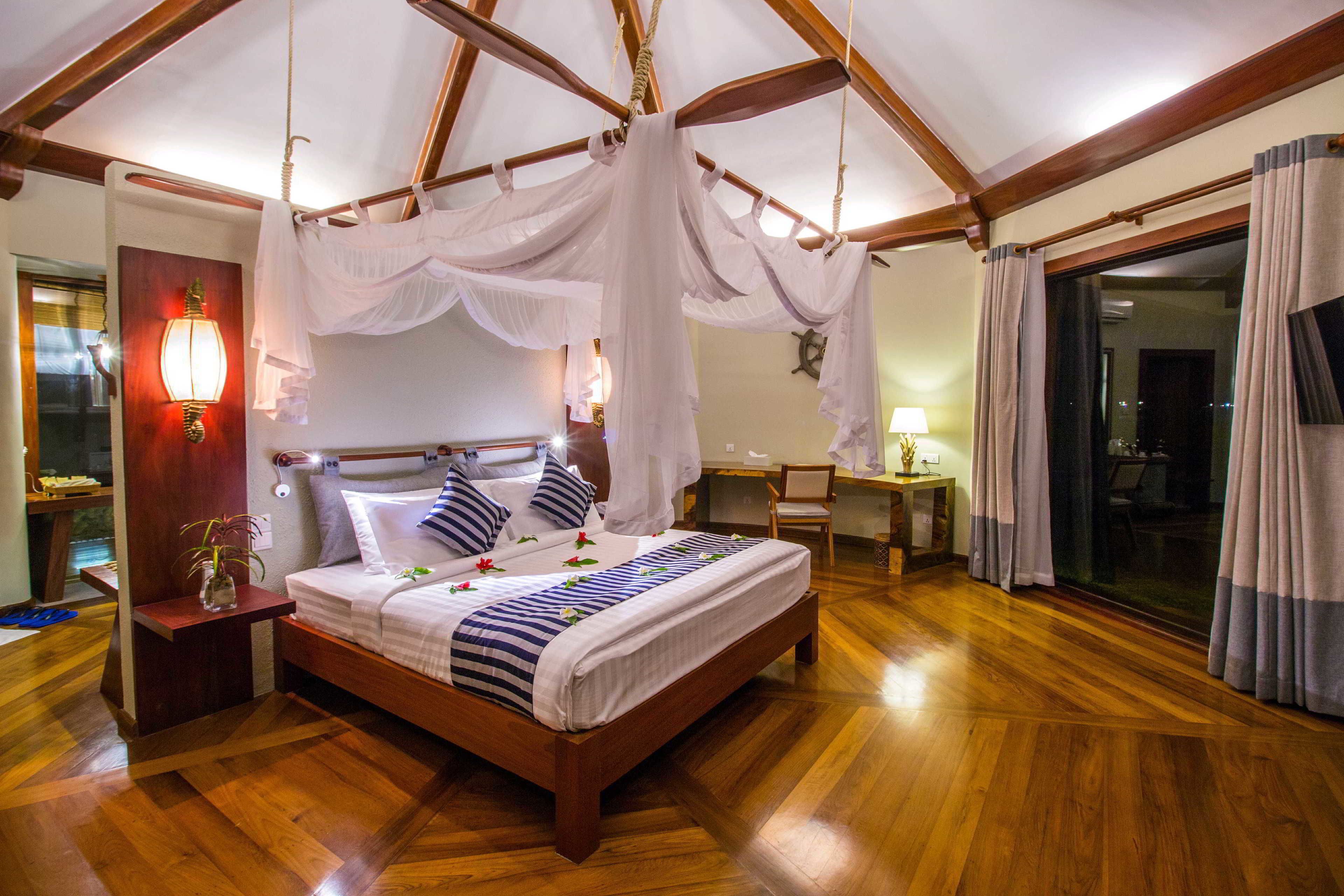 Un dormitorio espacioso con cama de madera, dosel, mesita de noche y vistas al exterior a través de un amplio ventanal.