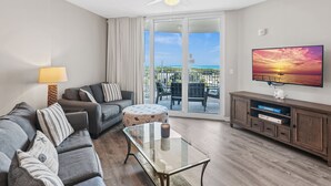 Un salon comprenant un canapé, un pouf, une table basse et un téléviseur posé sur un meuble en bois.