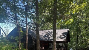 A wooden cabin with a porch, surrounded by trees.