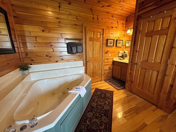 Interior de una cabaña de madera con una bañera grande, paredes de madera y una pequeña cocina.