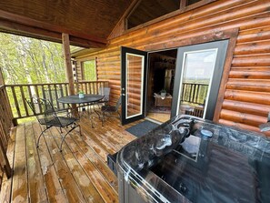 Una cabaña de madera con jacuzzi, un comedor con mesa y sillas, y vistas del bosque circundante.