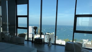 A modern living room with large windows, a sofa, a coffee table, and a view of the sea and city skyline. - The Base Central Pattaya by Minsu (Pattaya)