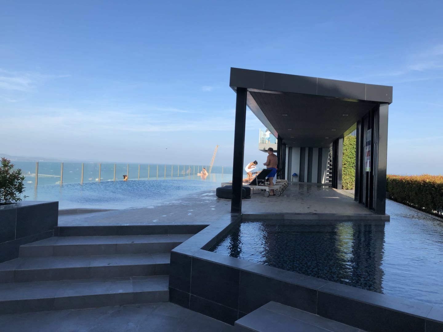 An infinity pool with a view of the sea, a covered seating area, and steps leading to the pool.