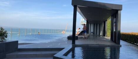 An infinity pool with a view of the sea, a covered seating area, and steps leading to the pool.