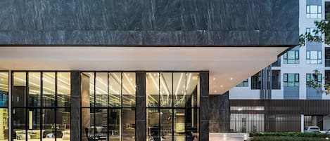 A modern building with large glass windows, a dark facade, and a well-lit entrance area with outdoor seating.