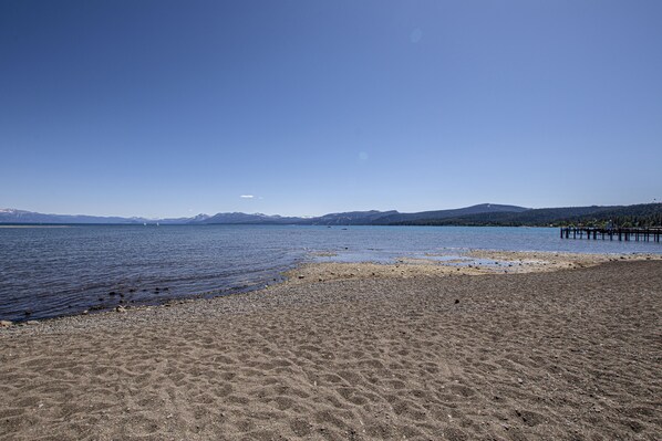A beach with a clear sky, calm water, and distant mountains.