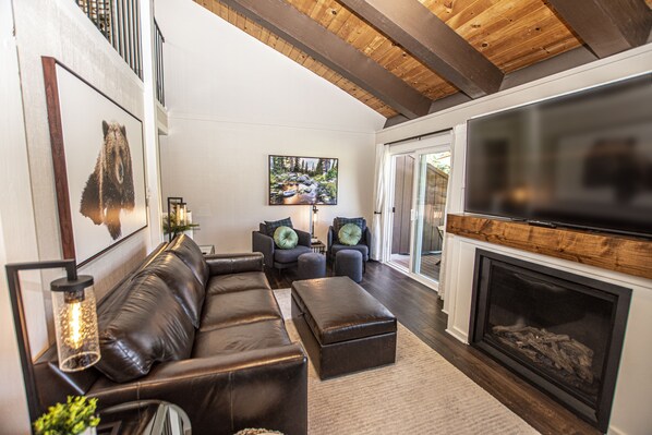 A modern living room with a leather sofa, two armchairs, a fireplace, and a large TV.