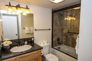 A bathroom with a sink, mirror, toilet, and shower area.