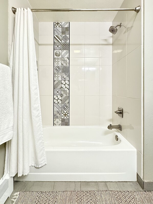 A modern bathroom with a white bathtub, a shower, and a patterned tile backsplash. - Walnut Mews - Quiet Creekside townhome next to Pearl Street (Boulder)