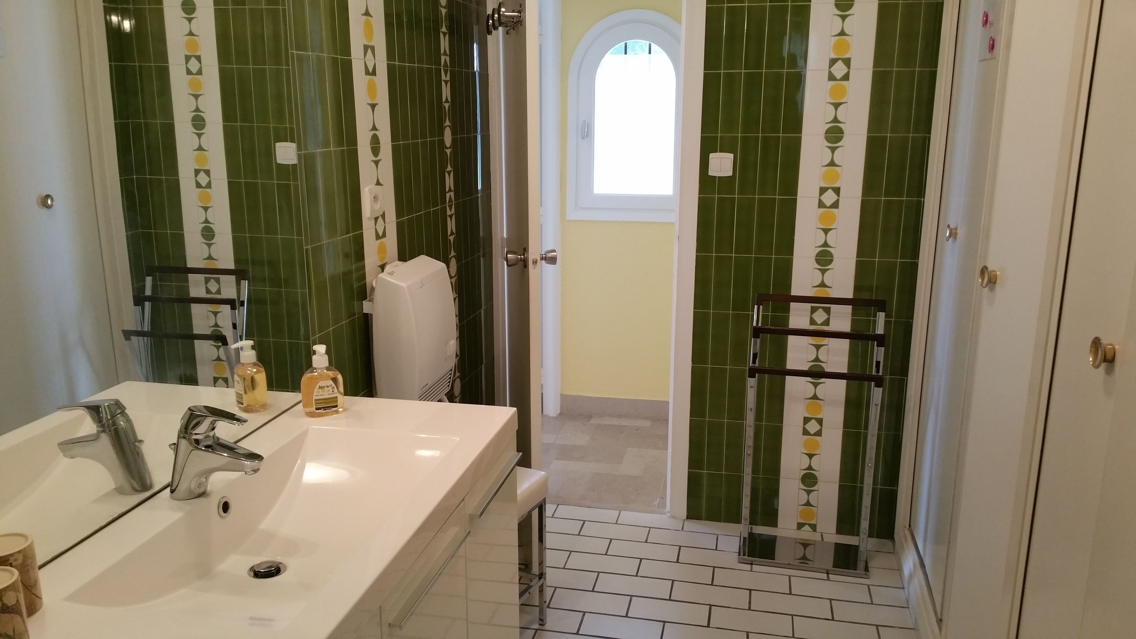 A bathroom with a large sink, two hand soap dispensers, a towel rack, and a shower area with a glass door.