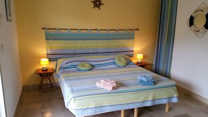 A hotel room with a striped bedspread, two bedside lamps, a ship's wheel decoration, and a life buoy sign on the wall. - Al Pati (Sorede)