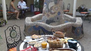 An outdoor dining area with a mosaic fountain centerpiece, surrounded by tables and chairs. - Al Pati (Sorede)