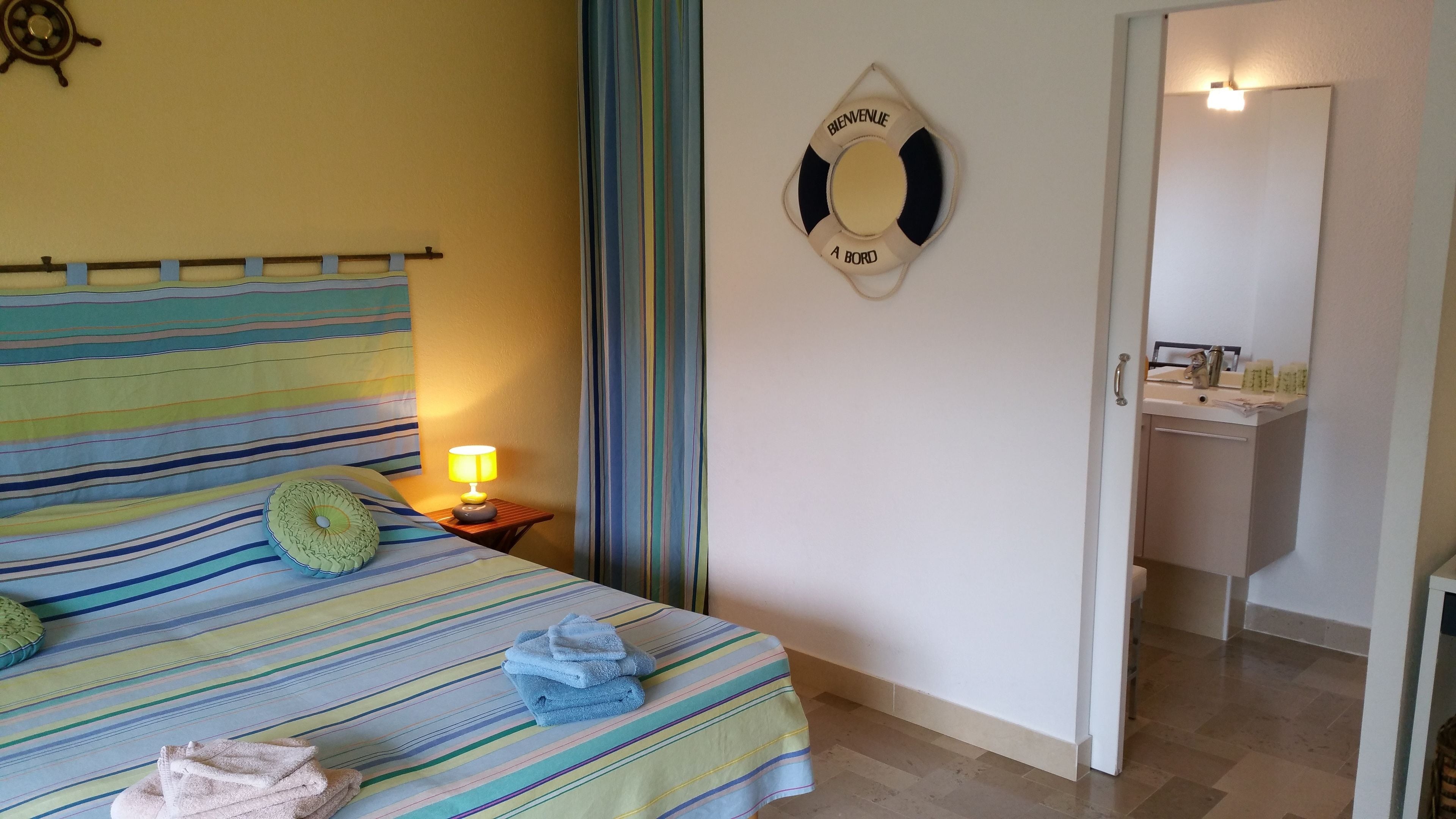 Une chambre d’hôtel avec un lit recouvert d’une courtepointe à rayures, une lampe de chevet et un panneau indiquant la présence d’un gilet de sauvetage fixé au mur.