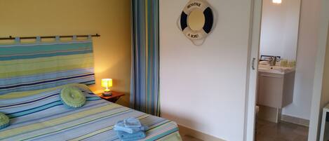 Une chambre d’hôtel avec un lit recouvert d’une courtepointe à rayures, une lampe de chevet et un panneau indiquant la présence d’un gilet de sauvetage fixé au mur.