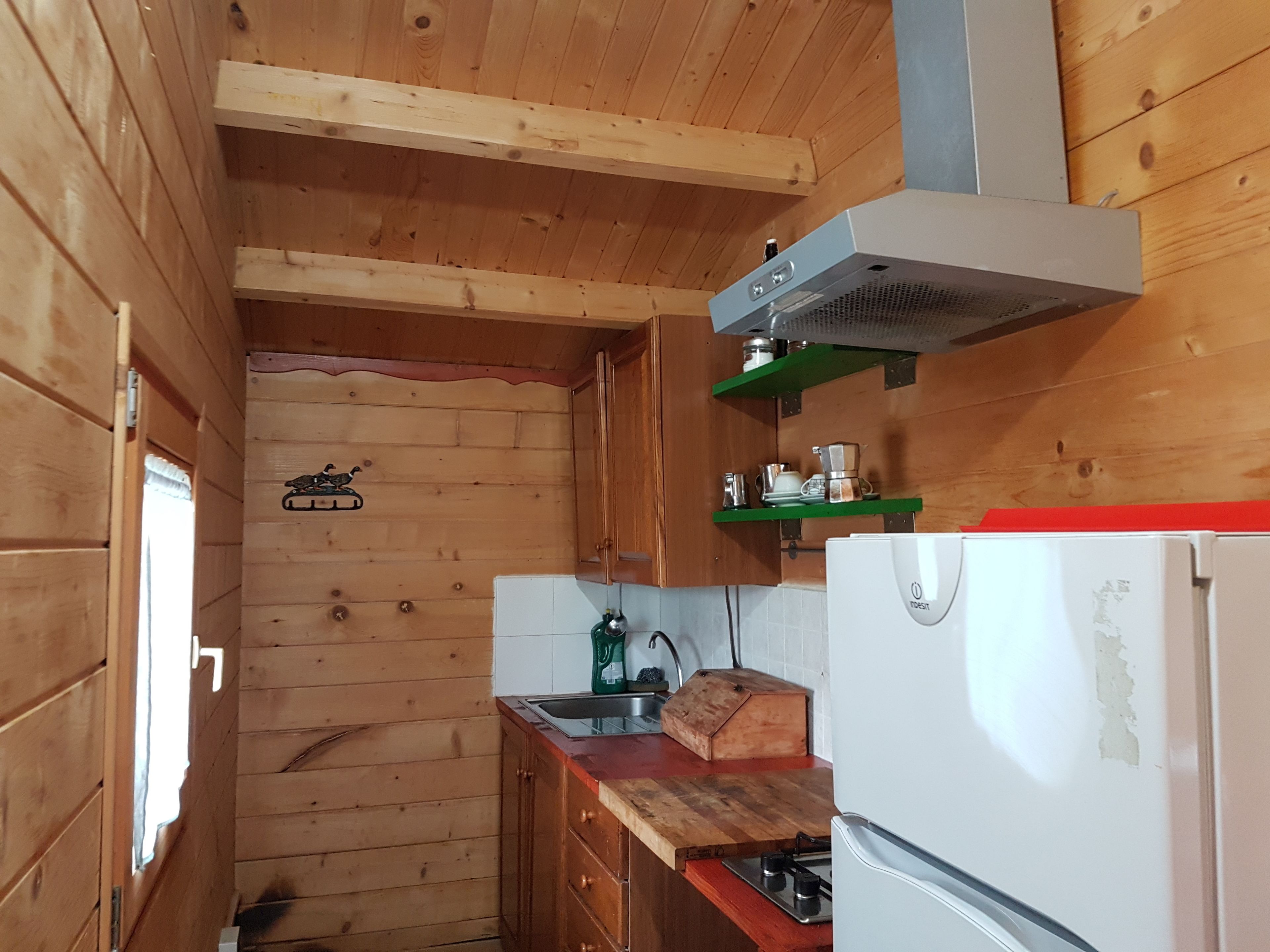 A compact kitchen with wooden walls, a built-in stove, a sink, and a refrigerator.