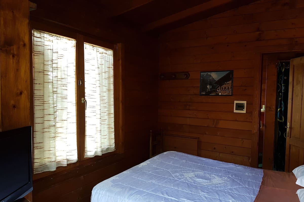 Ein Zimmer in einer Holzhütte mit einem Bett, einem Fernseher und einem Fenster mit Vorhängen.
