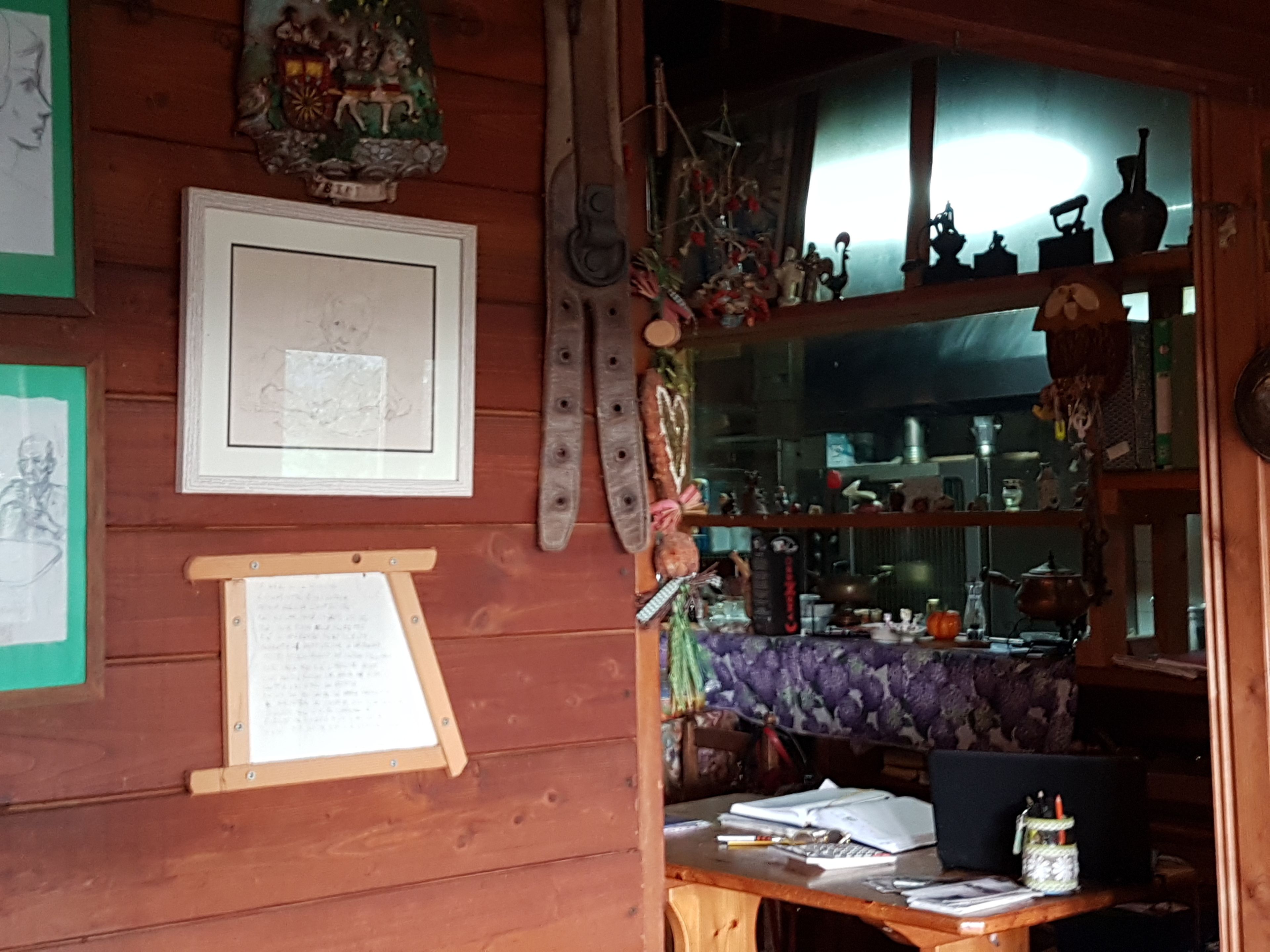 Una habitación rústica de madera con un escritorio, obras de arte enmarcadas y diversos utensilios de cocina.