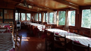A cabin with multiple wooden tables and chairs, large windows, and a wooden ceiling. - Agriturismo Cisogna (Anagni)