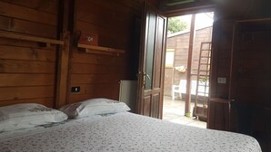 A wooden room with a bed, a radiator, a shelf, and an open door leading outside. - Agriturismo Cisogna (Anagni)
