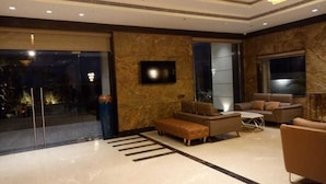 A modern lobby with a marble floor, leather sofas, a flat-screen TV, and a large window. - Hotel Parador (Firozabad)