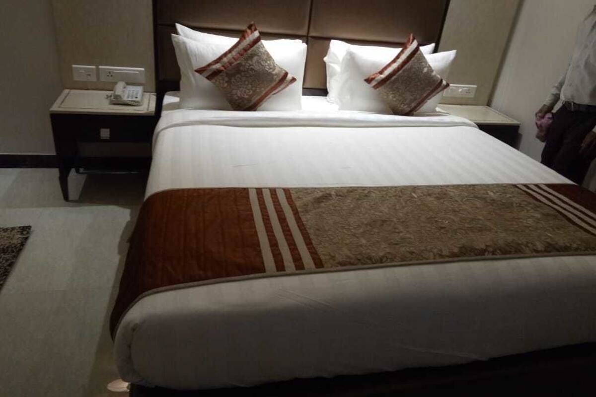 A hotel room with a large bed, a nightstand with a phone, and a headboard with a padded design.