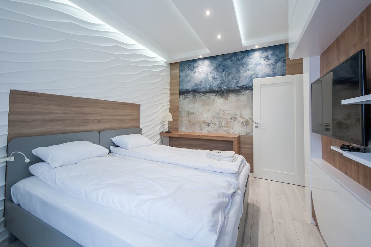Une chambre moderne avec un grand lit, des tables de chevet, une télévision et un mur au revêtement original.