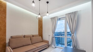 A modern living room with a beige sofa, a small table, and a view of the city through large windows.