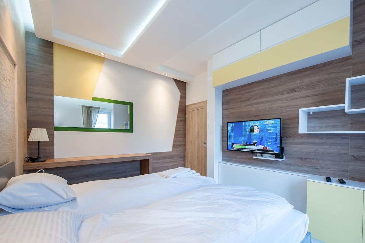 Une chambre d’hôtel moderne équipée d’un lit, d’un téléviseur fixé au mur, d’un miroir et d’une table de chevet avec une lampe.