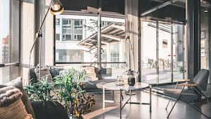 A modern living room with a sofa, coffee table, and chairs. There are large windows with a view of buildings and a balcony. - Four Points Flex by Sheraton Aalborg (Aalborg)