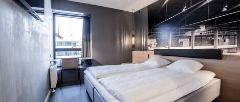 A modern hotel room with a large bed, a desk, and a view of the city.