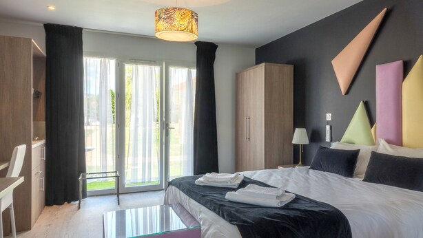 A modern hotel room with a large bed, a desk, and a view of the outdoors. - Domaine des Pierres Dorées (Ternand)