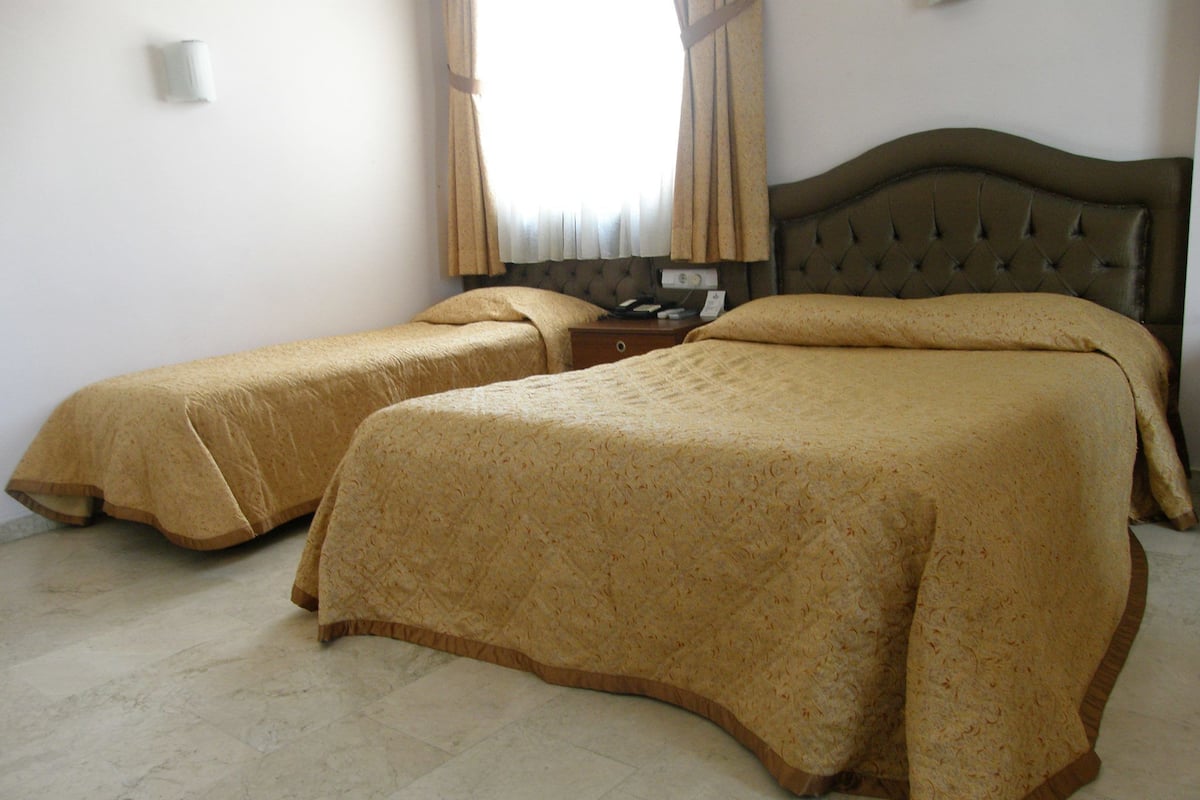 A hotel room with two beds, a wooden headboard, a nightstand, and a window with curtains.