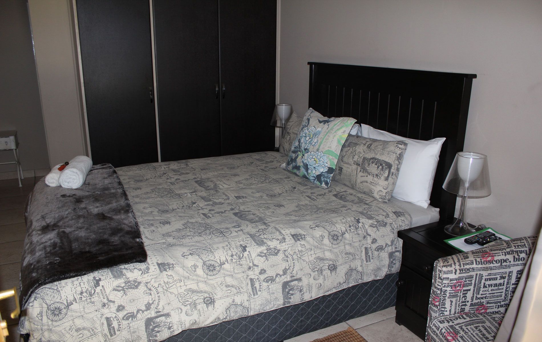 A neatly arranged bedroom with a bed, a nightstand, a lamp, and a chair.