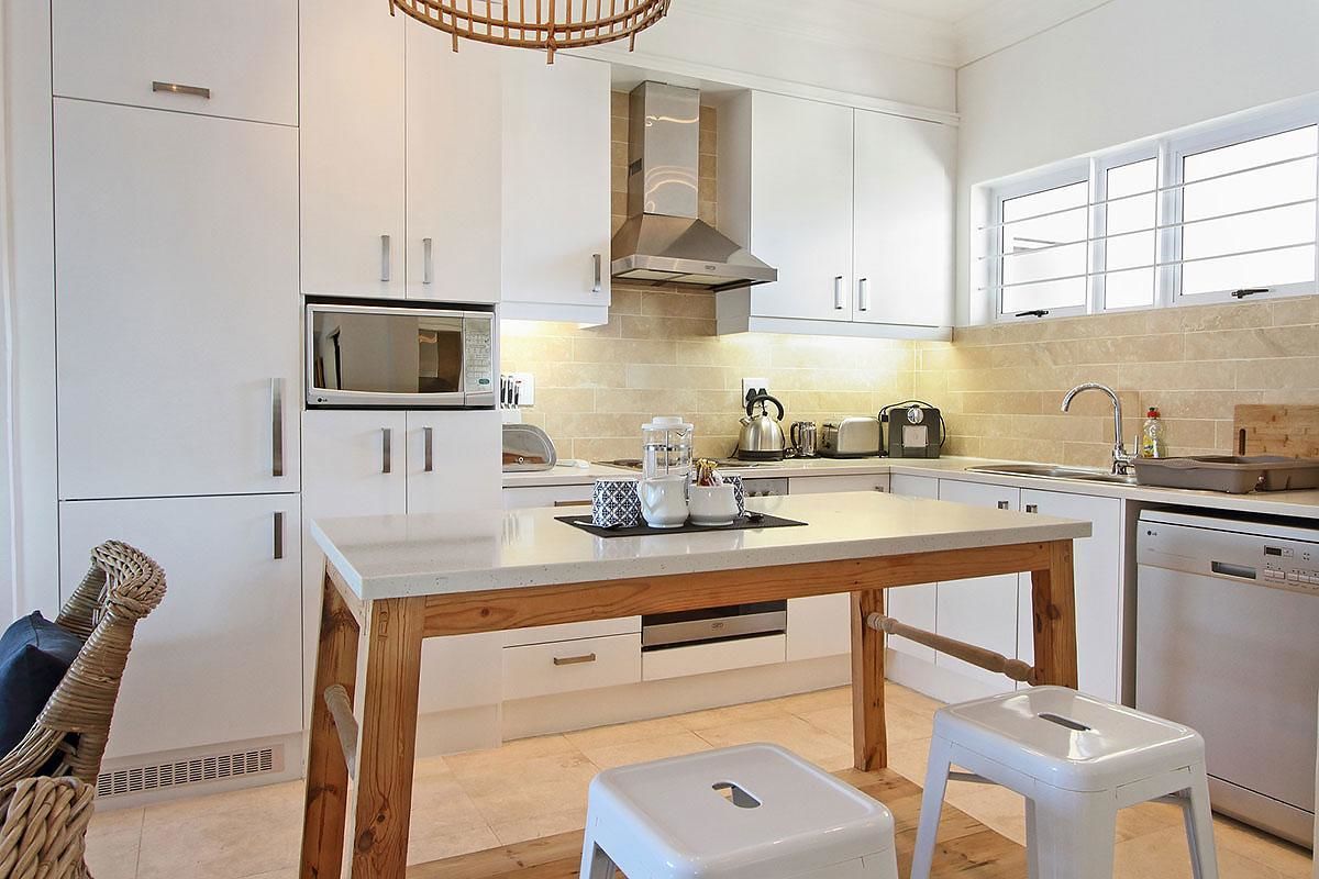 A modern kitchen with white cabinetry, a wooden island, a microwave, a kettle, and a dishwasher.