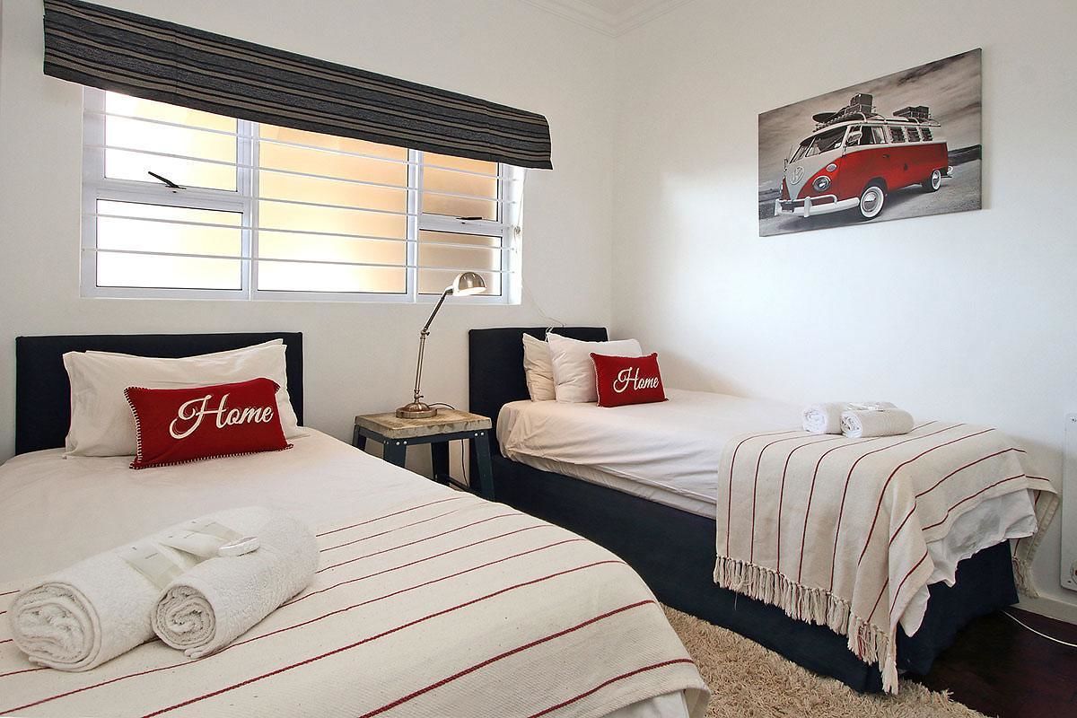 Una habitación de hotel con dos camas, una ventana con persianas, una lámpara y un cuadro de una furgoneta en la pared.