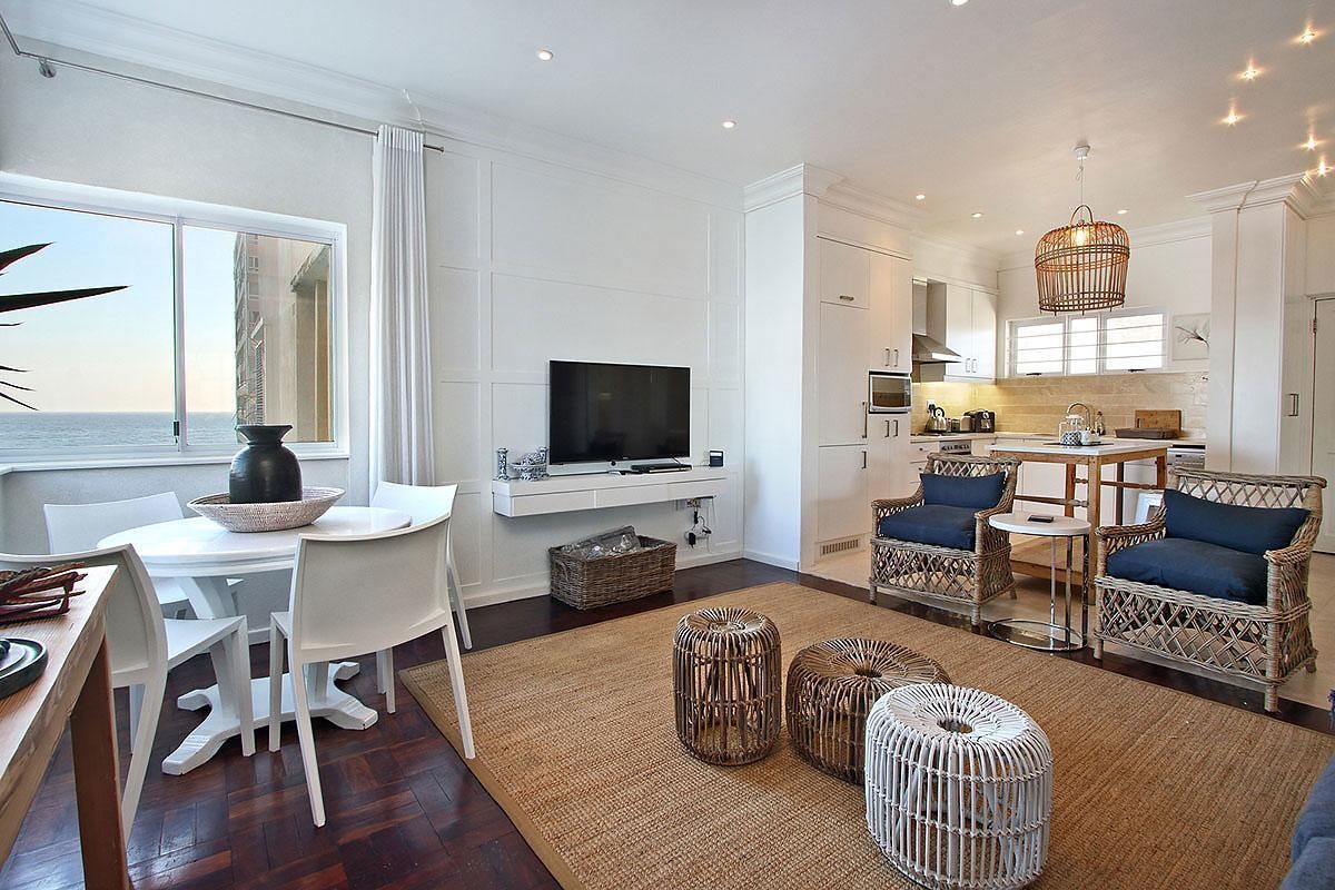 A modern living room with a dining area, a kitchen, and a large window offering a view of the sea.