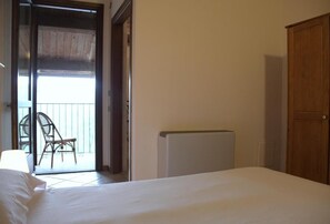 A bedroom with a bed, a radiator, a wooden wardrobe, and a sliding glass door leading to an outdoor area with a chair. - Locanda del Borgo (Prunetto)
