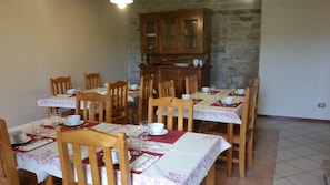 A dining area with wooden chairs and tables, each set with white plates, cups, and cutlery. A wooden cabinet is against the wall. - Locanda del Borgo (Prunetto)