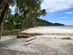 A beach with a swing, palm trees, and a sandy shore. - The Sunshine Resort (Ko Kood)