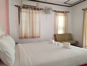 Quarto de hotel com uma cama, um sofá verde, um ventilador e cortinas.