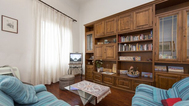 A living room with two striped sofas, a coffee table with a patterned tablecloth, a wooden bookshelf filled with books, a television on a stand, and a framed picture on the wall. - Proconsolo (Florence)