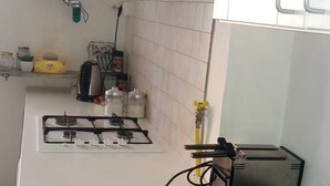Una cocina con estufa a gas, cafetera y hervidor. Hay un calendario en la pared y una ventana con persianas.