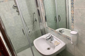A bathroom with a glass-enclosed shower, a white sink, and a mirror. - Rumariya Rooms Hostel (Rome)