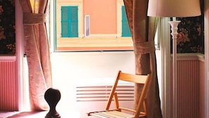 Una habitación con cama, una silla, una lámpara y vistas a edificios a través de cortinas.